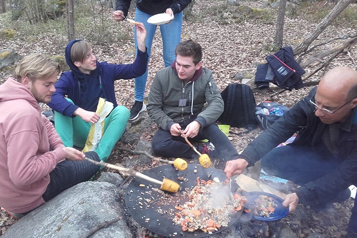 Students sitting outside making dinner over an open fire.