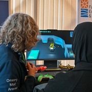 En elev och en verksam i yrkeslivet står med ryggarna vända mot kameran och tittar på en skärm med ett CAD-program.