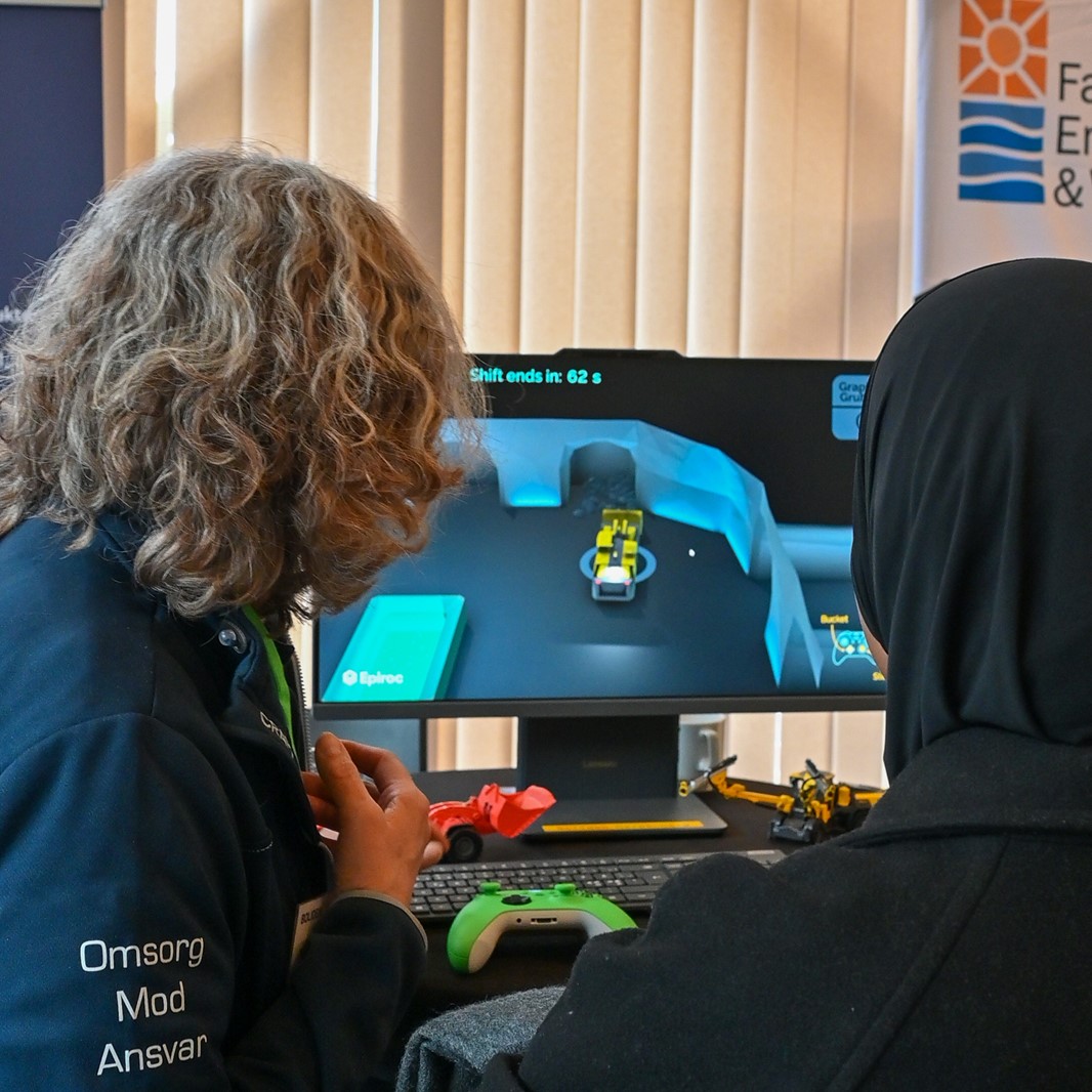 En elev och en verksam i yrkeslivet står med ryggarna vända mot kameran och tittar på en skärm med ett CAD-program.