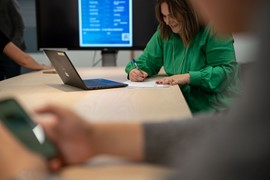 Personer som sitter vid datorer runt ett mötesbord.