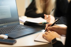 Personer som skriver vid en dator och på ett anteckningsblock