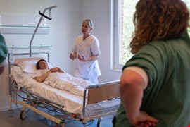 Person som ligger i en sjukhussäng. En person står bredvid och pratar.