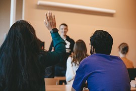 Flera studenter sitter i ett klassrum i rader och lyssnar på en föreläsning.