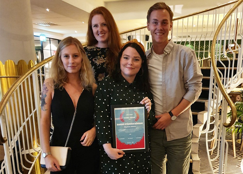 The award winners, three women and one man, pose on a flight of stairs, with one of the female students holding the award, a diploma in her hand.