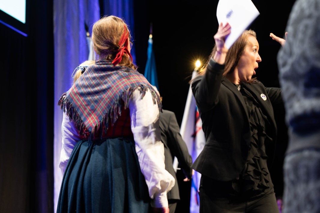 Två personer som står brevid varandra, personen till höger räcker upp händerna iluften av lycka och har ansiktet mot kameran. 