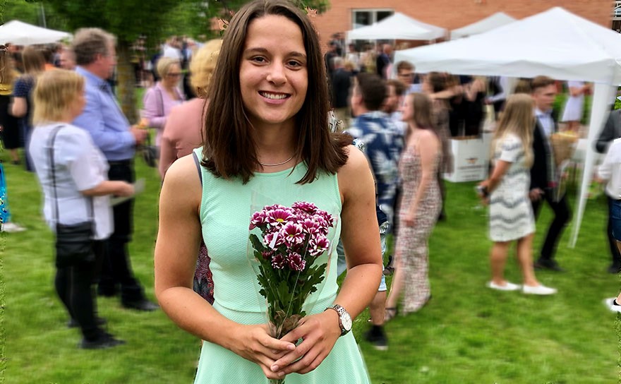 Alina Johansson holding onto a bouquet of flowers, standing outside on a lawn with other ceremony attendees.