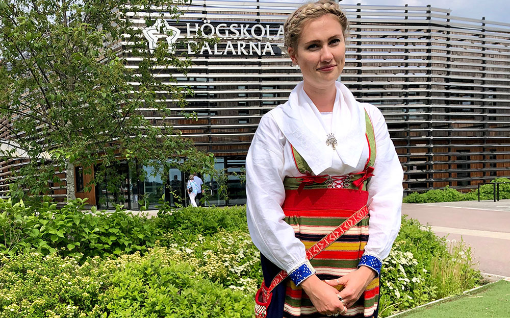 Linnea Höglund in folk costume standing outside Campus Falun