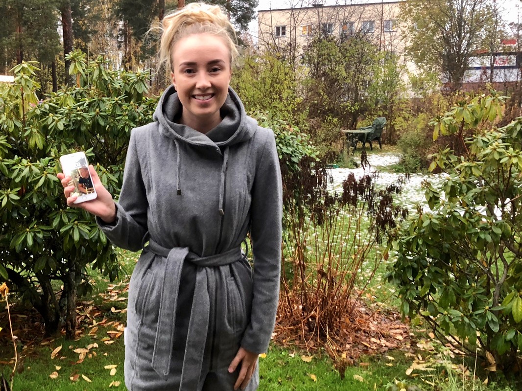 Ida standing outside in front of bushes with a mobile phone in her hand.