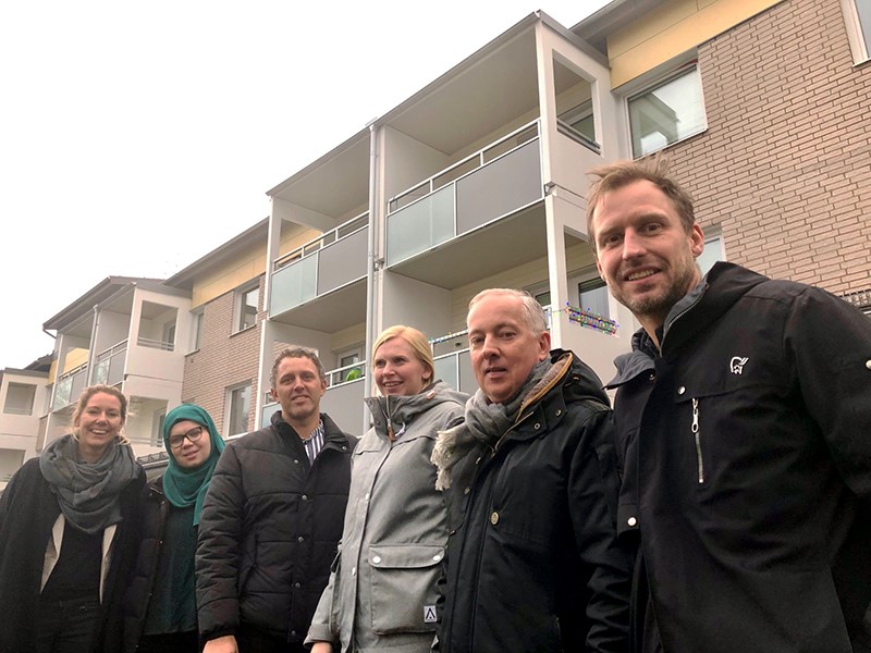 Three women and three men standing outside in front of an apartment building