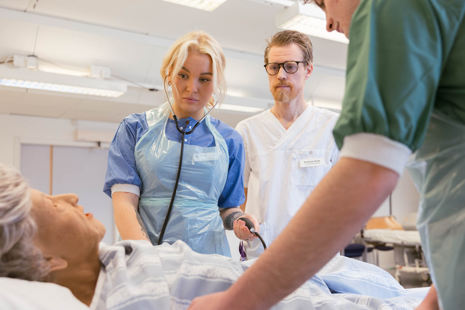 Studenter genomför en praktisk vårdövning med en patientdocka i en klinisk undervisningsmiljö.