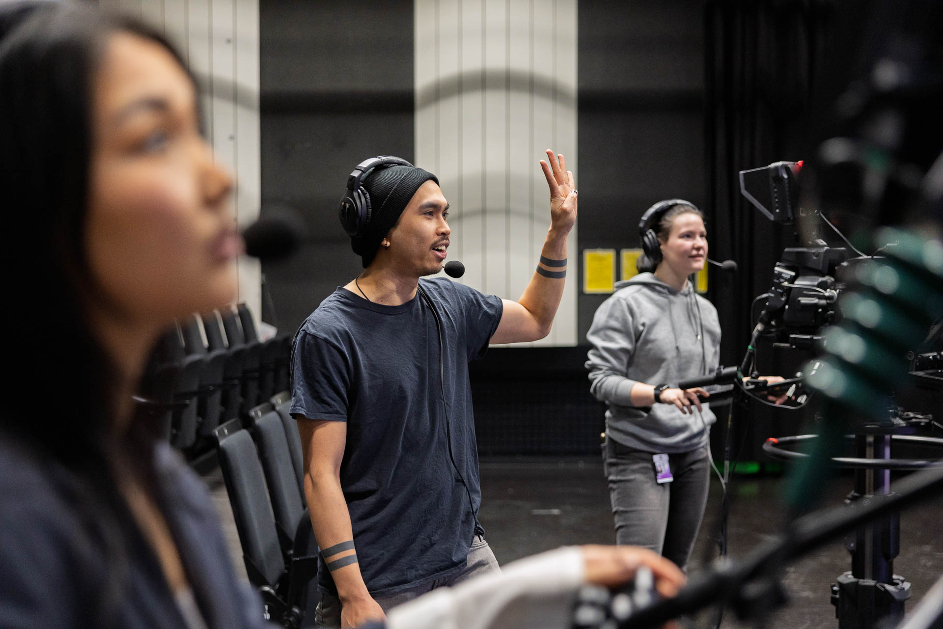 Tre personer arbetar med en inspelning i en studio. En person gestikulerar medan övriga medverkar framför kamerautrustningen.