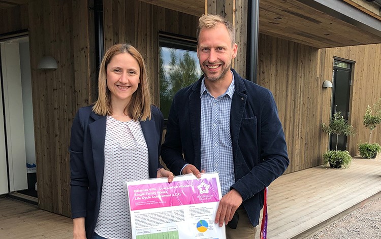 A woman and man standing outside the new Dalarnas Villa holding onto the drawing plans.