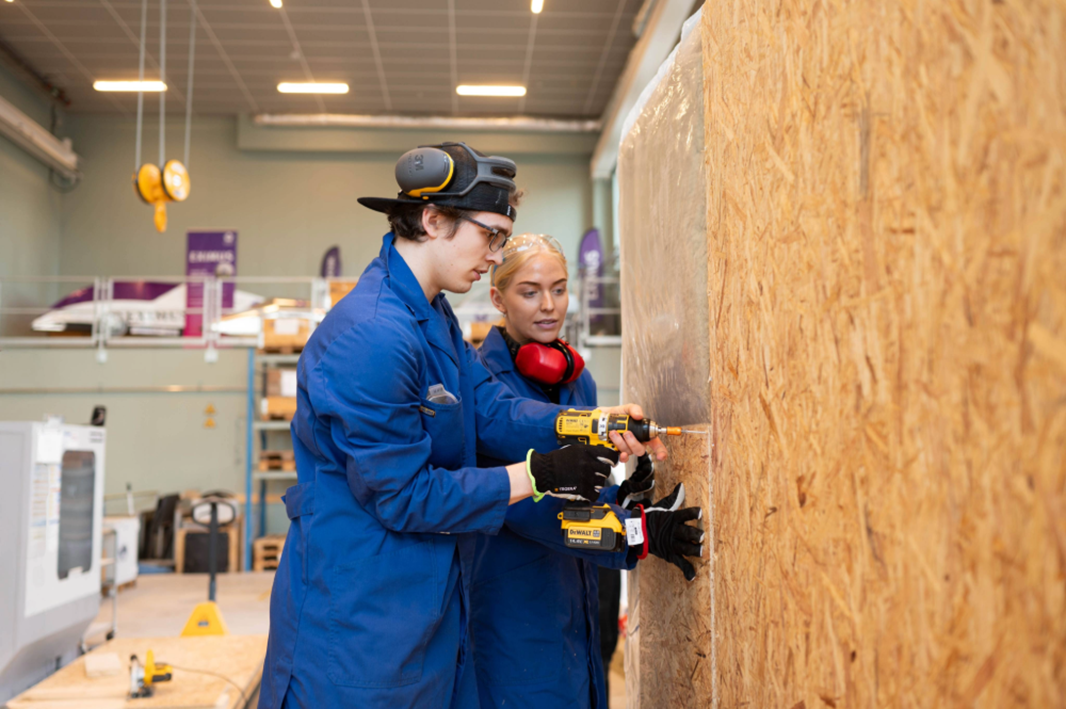 Två studenter står och skruvar i en vägg. 