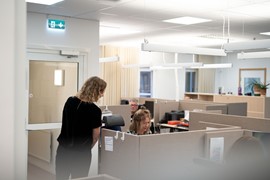 En person sitter vid ett skrivbord. En annan person står bredvid.