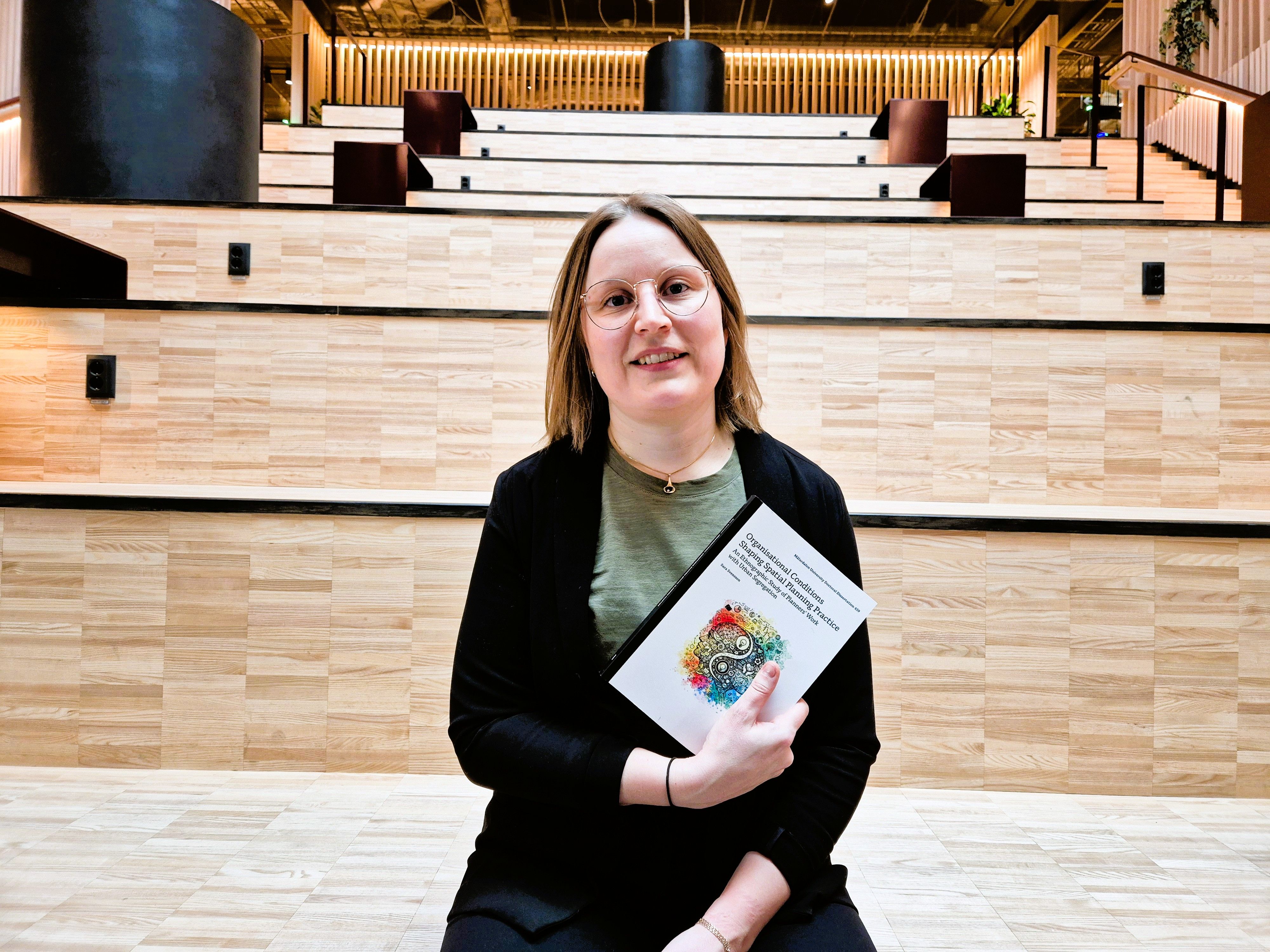 Person sittande p&aring; trappor med sin doktorsavhandling