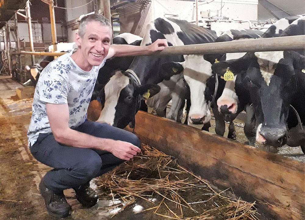 Professor Lars Rönnegård crouching down in front of a row of cows in a barnyard.