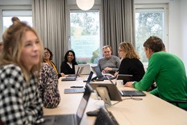 En grupp människor som sitter runt ett bord med bärbara datorer.