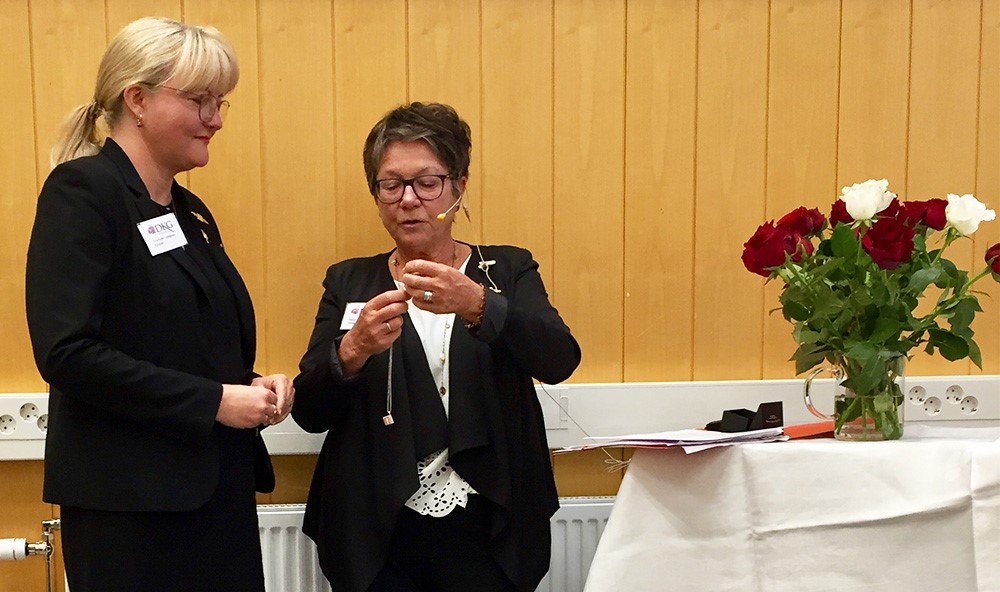 Charlotte Lindgren, till vänster, tar emot ett smycke i silver av kommitténs ordförande Helga Skeidsvoll.