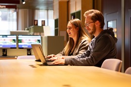 En man och en kvinna sitter vid ett bord med en bärbar dator och studerar i ett bibliotek.