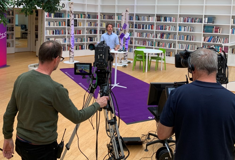 Två kameramän filmar Mikael Swaréns föreläsning i ett bibliotek.