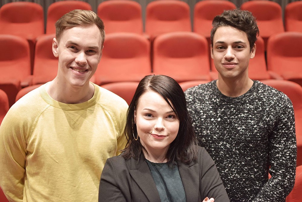 Three students in a theatre, with the seats behind them.