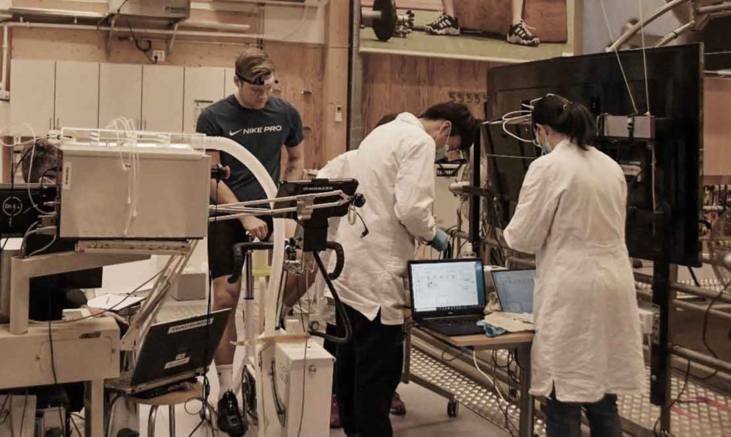 Man på motionscykel och två personer i labbrock