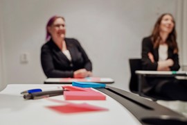  Block och penna i förgrunden två personer suddiga i bakgrunden