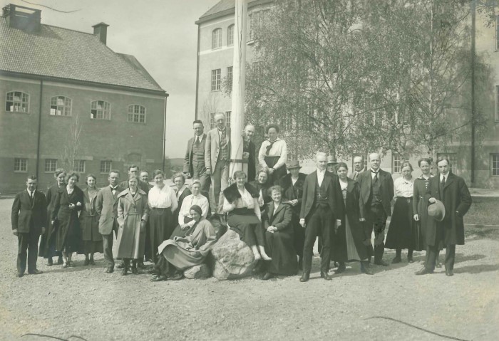 Äldre bild på lärarkollegiet framför en flaggstång. 