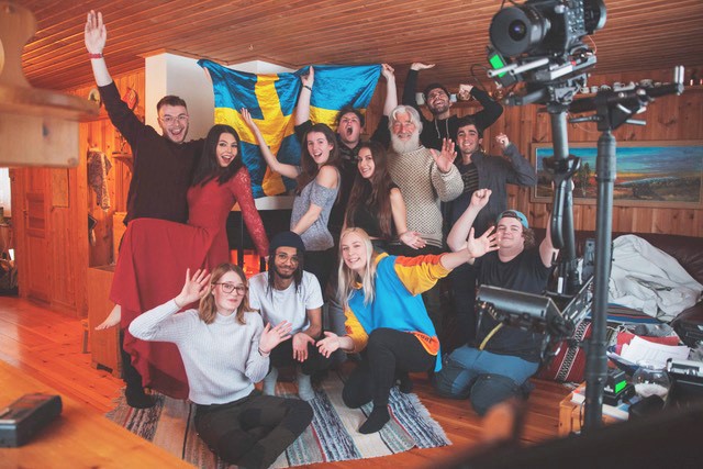 Students gathered in front of a Swedish flag in a room in a Swedish cottage