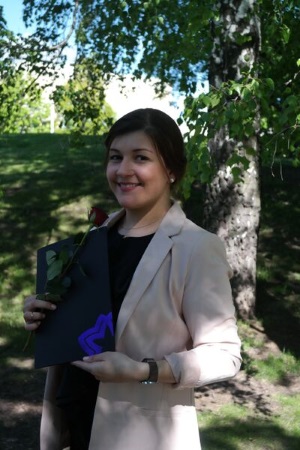 Student standing at graduation with trees and sun behind her