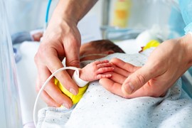 Hand och ett för tidigt fött spädbarn på en intensivvårdsavdelning (IVA) på sjukhus, med monitor