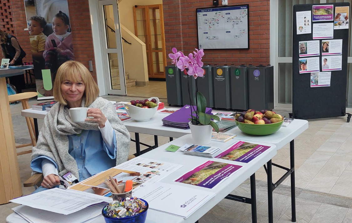 Kvinna sitter vid entren och vid ett bort där det ligger böcker och där det står en blomma