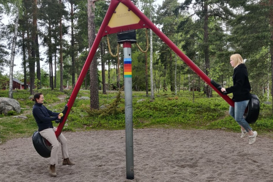Studenter på sitter på snurrgunga på lekplats. 