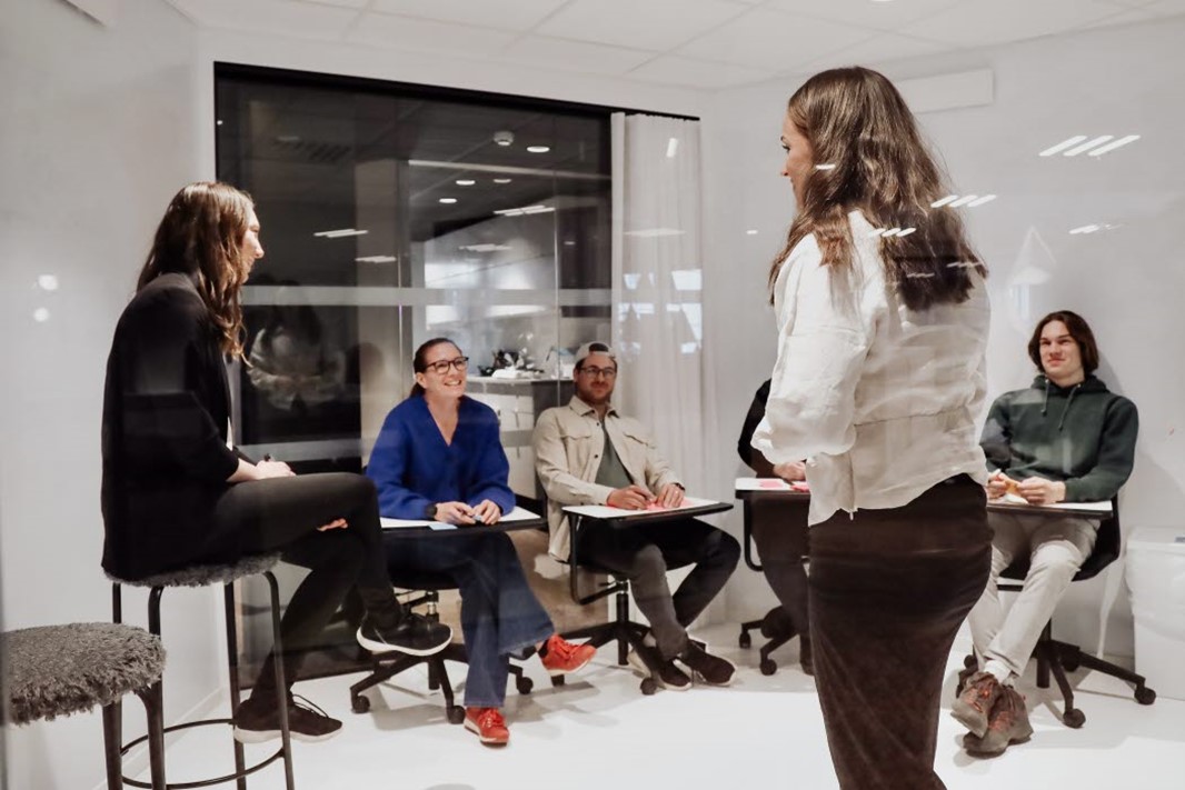 Grupp personer inomhus lärosal sitter står