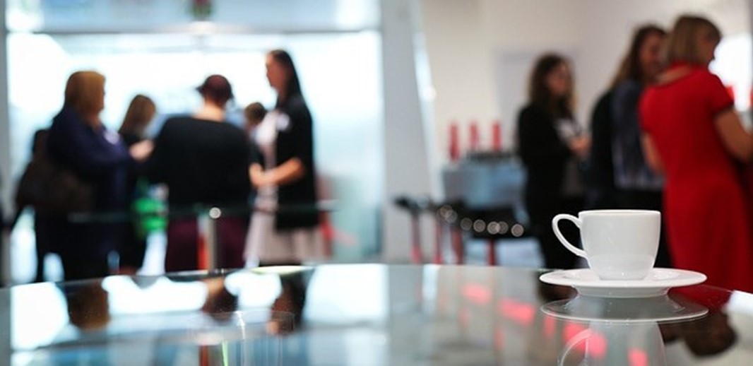 Fokus på förgrunden med ett bord med en kaffekopp, i bakgrunden står ett antar personer utan fokus