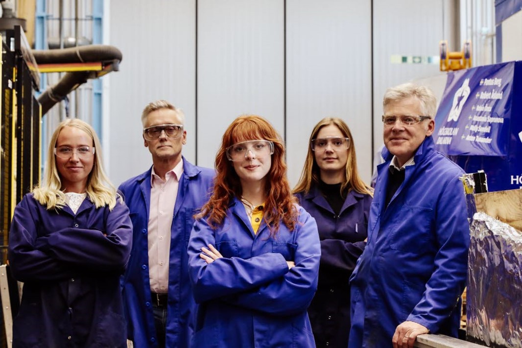 Grupp med fem glada personer står inomhus verkstad skyddsglasögon.