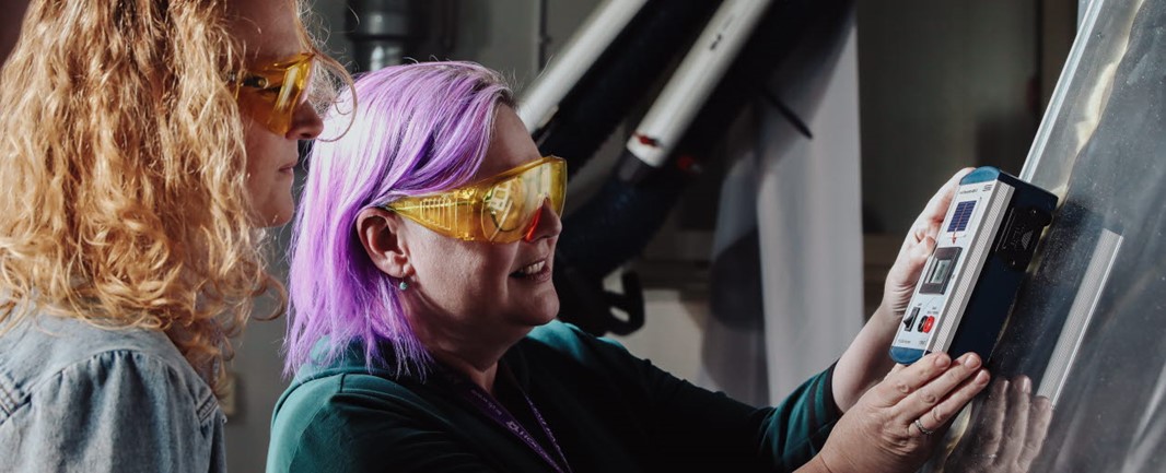 Two persons with protective glasses stand indoors in front of measuring panel laboratory for solar simulation