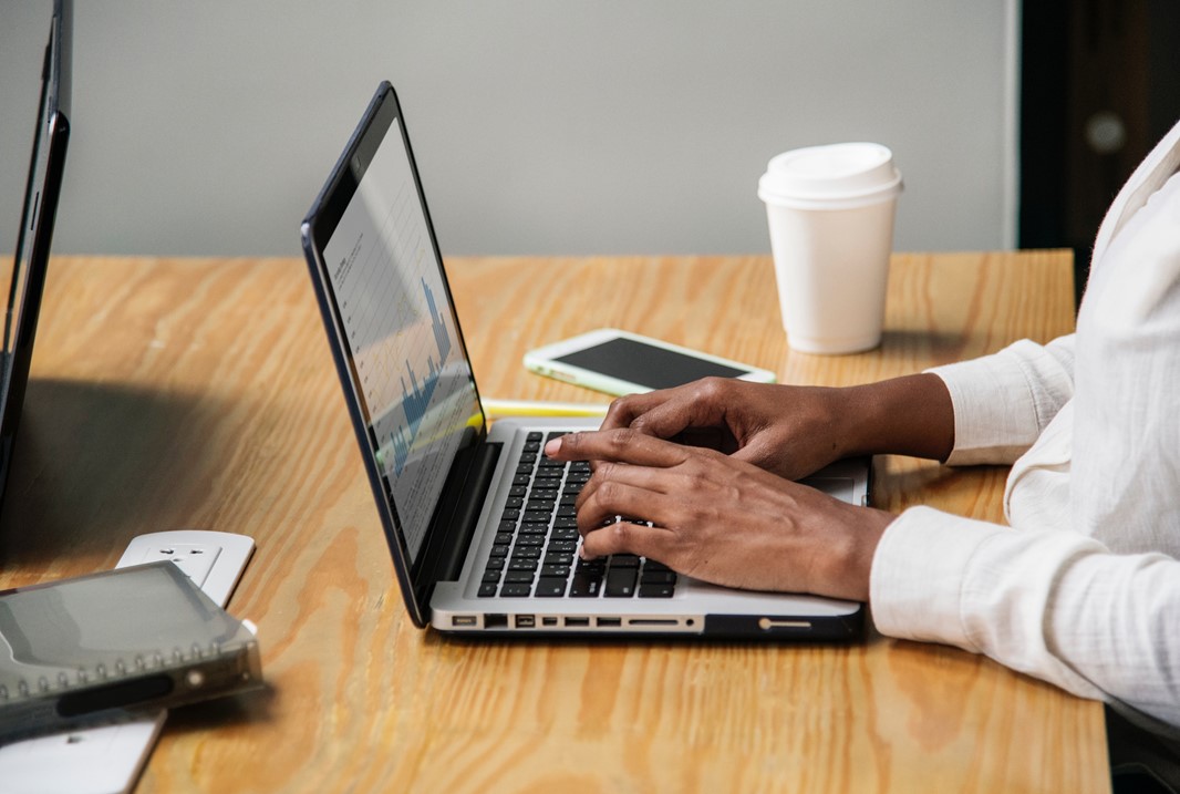 Man som skriver på laptop. I bakgrunden syns en kaffekopp och en mobiltelefon. På skärmen skymtar man statistik och ett Foto av rawpixel på Unsplash.