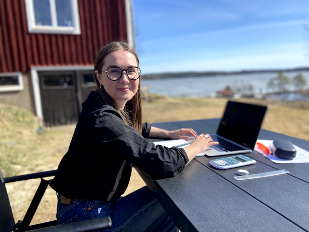 Emelie sitter med en bärbar dator vid en uteplats