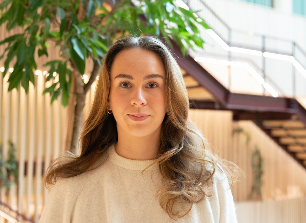 Porträttbild på Annie där hon tittar in i kameran och ler. I bakgrunden ser man Kunskapstrappan på campus Borlänge.